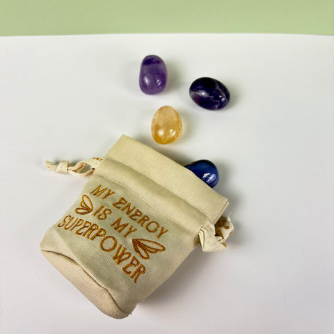 Small cream canvas drawstring pouch with gold embroidery and ruffled top, displayed with three polished crystals.