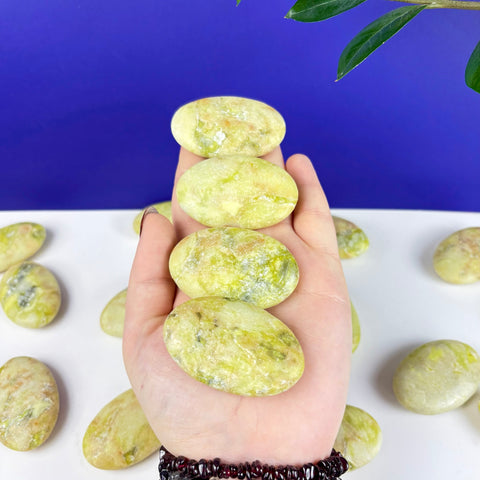 Hand holding four polished, oval-shaped Toxic Waste serpentine and mica palm stones with vibrant lime green and yellow hues.