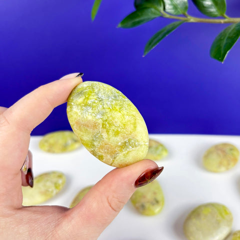 Hand holding a smooth, oval Toxic Waste serpentine and mica palm stone with vibrant yellow-green mineral patterns.