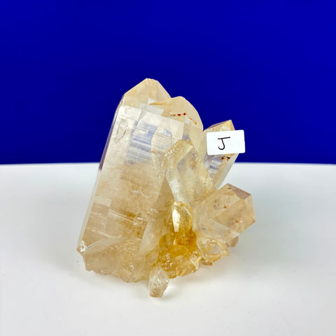 Clear Himalayan quartz crystal cluster with golden hues and sharp, pointed terminations on a white surface.
