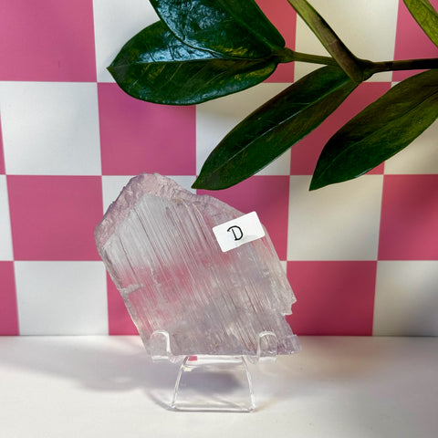 Vibrant pink Kunzite crystal variant D, displayed on a clear stand with a checkered background.