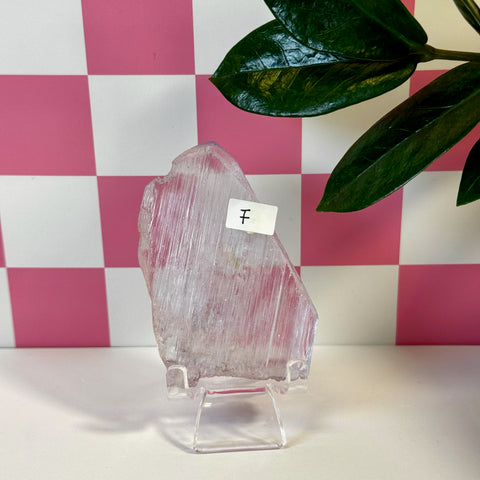 Vibrant pink kunzite crystal slab, variant F, on a clear stand with a checkered background.