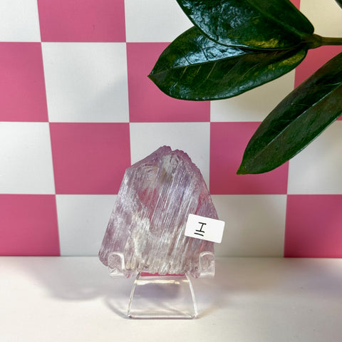 Vibrant pink Kunzite crystal on a clear stand, with a pink and white checkered background.
