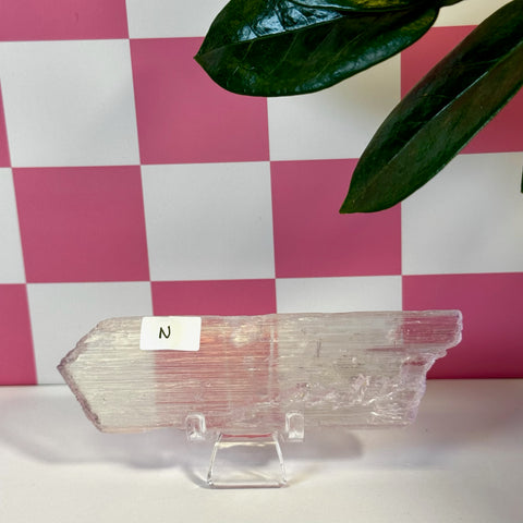 Vibrant pink kunzite crystal on a clear stand, with a pink and white checkered background.
