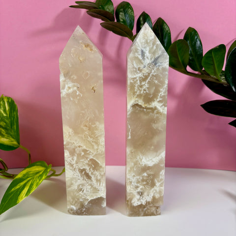 Two polished white feather agate towers with intricate crystalline patterns against a pink background.