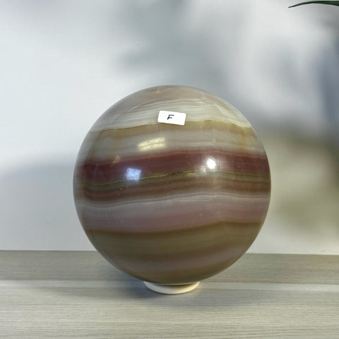 XL pink banded onyx sphere with natural variations, on a light wooden surface.