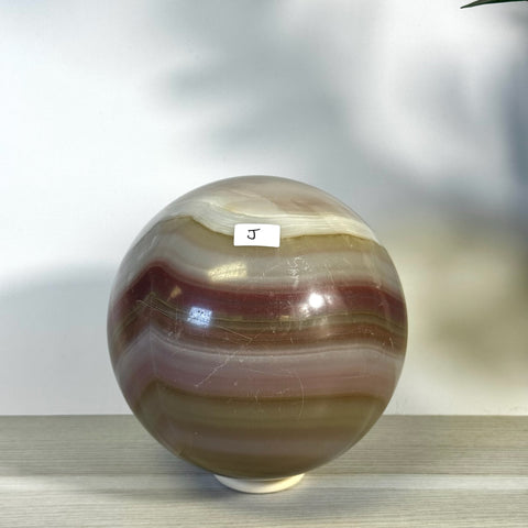 XL pink banded onyx sphere with natural white, brown, and deep red stripes, on a light surface.