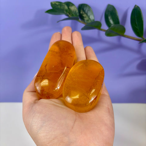Two smooth, polished yellow fluorite palm stones held in a palm against a purple background.