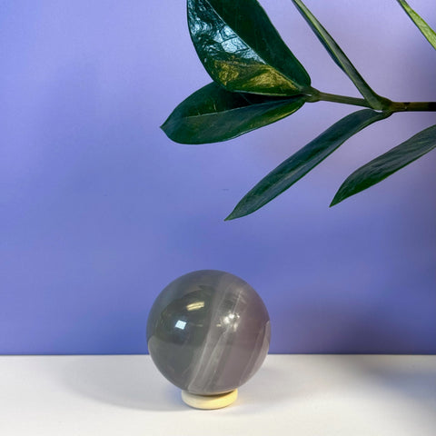 Smooth Yttrium Fluorite sphere with purple and grey bands on a light stand, against a purple wall.