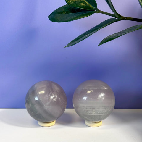 Two polished Yttrium Fluorite spheres on stands, displaying subtle purple and grey bands.