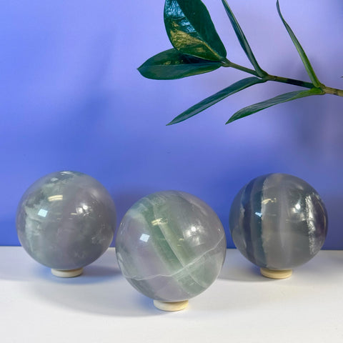 Three Yttrium Fluorite spheres on stands, displaying purple, green, and gray bands.
