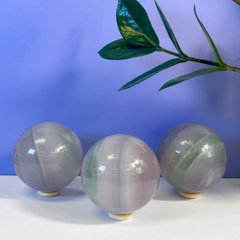 Three smooth Yttrium Fluorite spheres with purple, green, and white bands on stands.