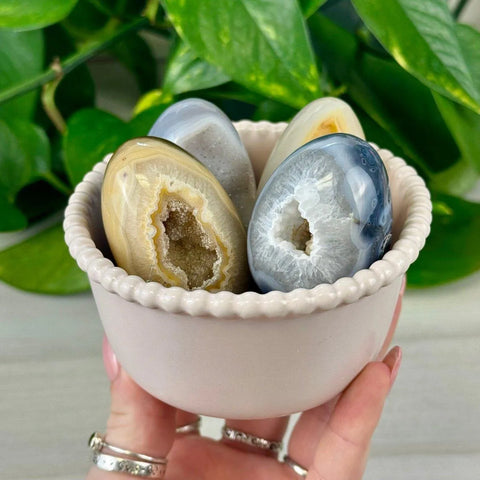 Polished geode eggs in natural blue, grey, and yellow tones, nestled in a light pink bowl.