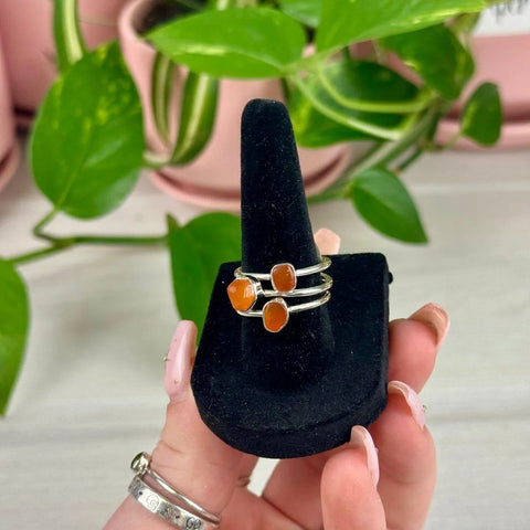 Sterling silver rings with vibrant orange carnelian stones on a black velvet display, July collection.
