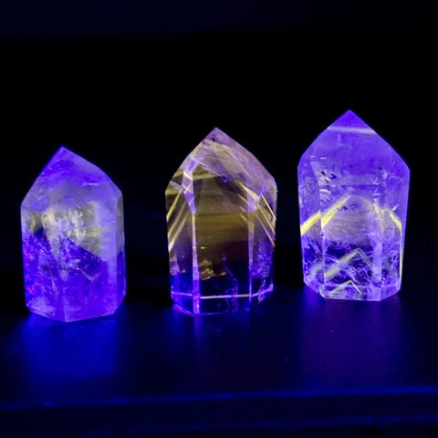Three glowing UV-reactive crystal towers, radiating purple and yellow light against a dark background.