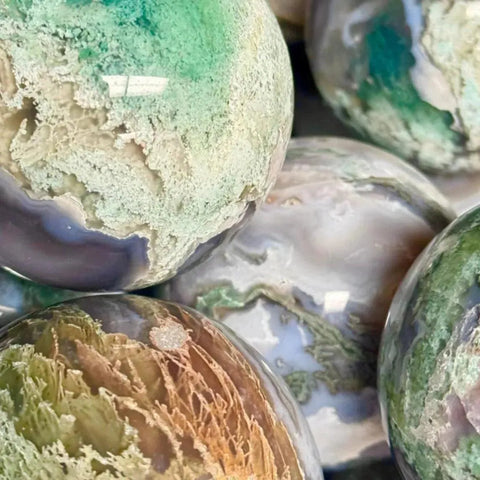 Polished moss agate spheres in varied green, white, brown, and purple hues with natural patterns.
