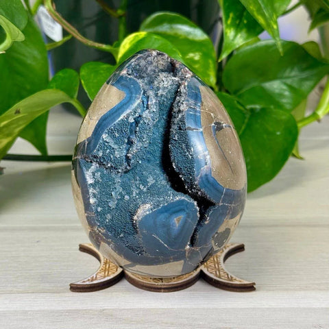 Phosphorescent blue and brown geode egg with sparkling crystals on a wooden stand.