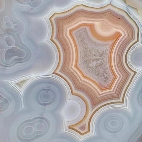 Close-up of a polished agate slice, revealing intricate white, gray, and warm orange-brown concentric bands.