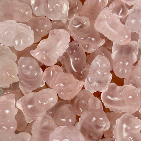 Pale pink rose quartz dinosaur carvings, smooth and translucent, filling the frame.