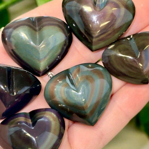 Polished rainbow obsidian hearts with iridescent green and purple bands held in a palm.