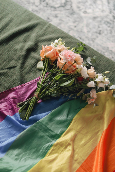 Vibrant Pride flag draped with a bouquet of peach roses and white flowers, symbolizing love and diversity.