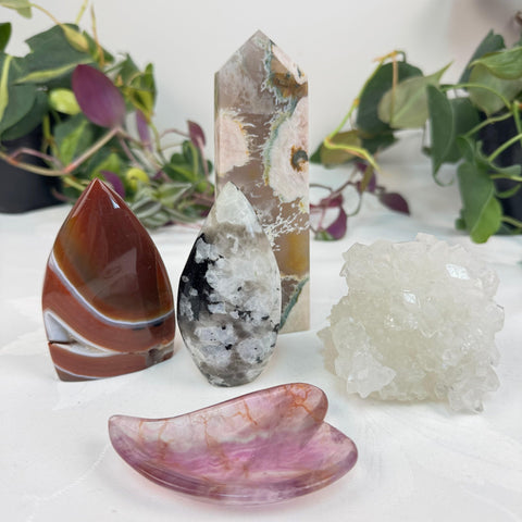 Assorted polished and raw crystals: red agate, cherry blossom agate tower, black moonstone, clear quartz cluster, and pink gua sha.