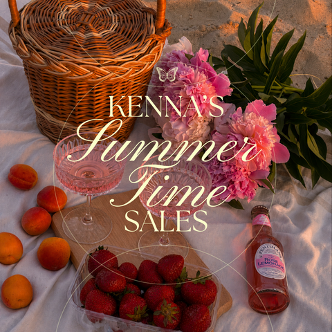 Wicker picnic basket, pink peonies, strawberries, and rose lemonade on a white blanket at sunset.