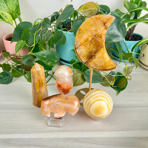 Warm orange and yellow crystal collection: moon, sphere, mushroom, and towers, surrounded by green plants.