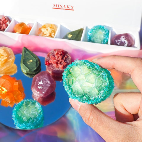 Colorful gummy candies being held with a tray of more candies in the background, featuring the brand 'MISAKY'.