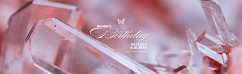 A close-up of clear faceted crystal structures with a soft pink and rose-toned blurred background. White script text in the center reads 'Kenna's Birthday' with smaller text below reading 'RESTOCK AUG 29TH' and '10:00 AM EST'.