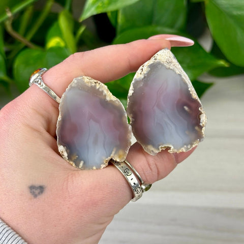 Two polished agate slices, gray and purple with natural rough edges, held in a hand.