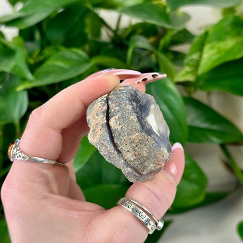 Rough gray agate pair with white banding, held against green foliage.