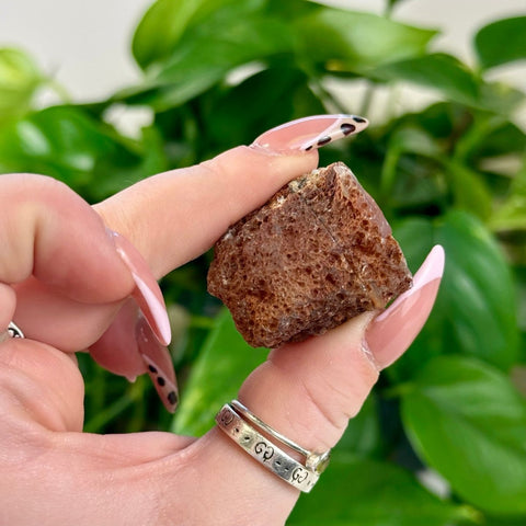 Rough brown agate crystal held between fingers with pink manicured nails.
