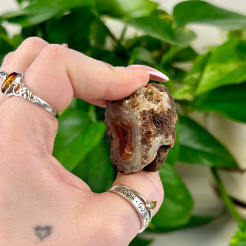 Hand holding a small, rough brown and white agate pair with an orange crystal center.
