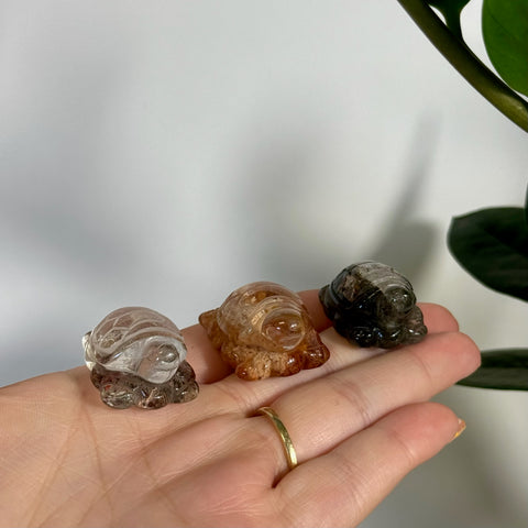 Three small, carved quartz turtle figurines in clear, amber, and dark brown, held in a hand.