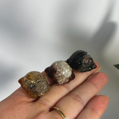 Three small, carved quartz turtles in varying translucent shades of brown, white, and dark green, held in a hand.