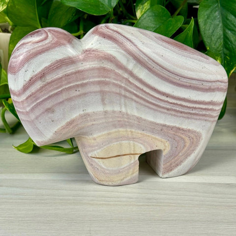 Andrea The Bison, a carved rainbow rhyolite figurine with swirling pink, purple, and white bands.