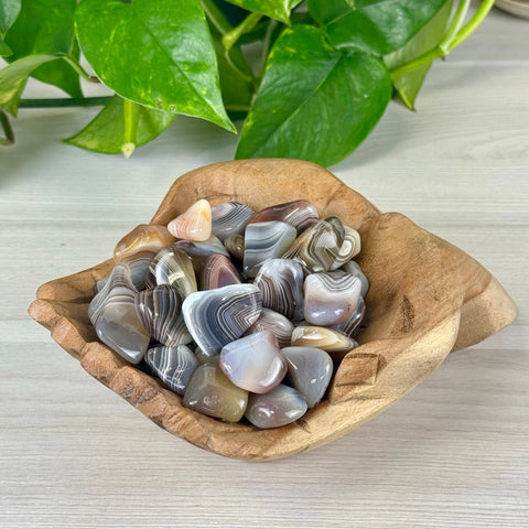 Smooth, polished banded Botswana agate tumbles in a natural wood bowl.