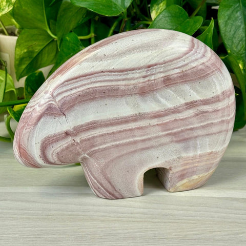 Becky The Bear carving, Rainbow Rhyolite, with pink and white wavy stripes, on a light wood surface.
