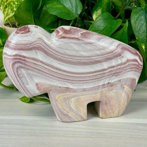Charlie The Bison carved from rainbow rhyolite, featuring swirling pink, white, and beige patterns.