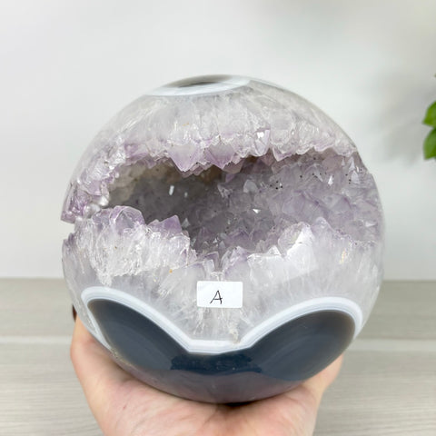 Polished amethyst geode sphere with banded black and white agate accents held in a hand.