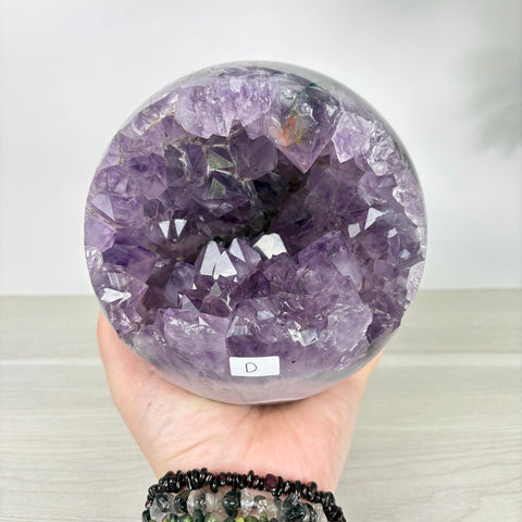 Handheld amethyst geode sphere with a deep purple crystal interior and polished agate outer shell.