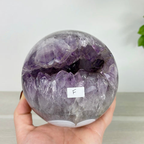 Polished amethyst geode sphere with a deep purple crystal center and banded agate base held in a hand.