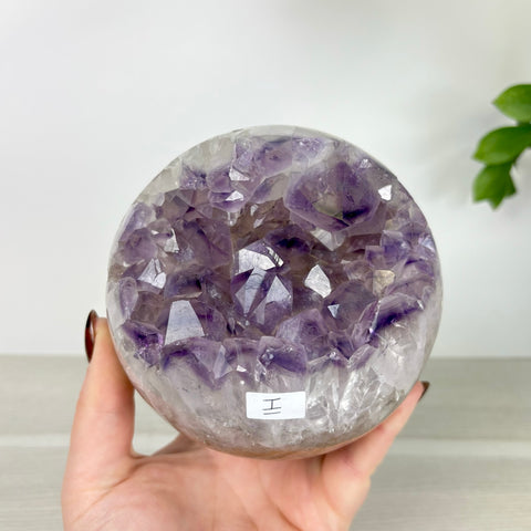 Handheld amethyst and agate chomp ball sphere featuring deep purple crystal clusters inside a polished stone casing.