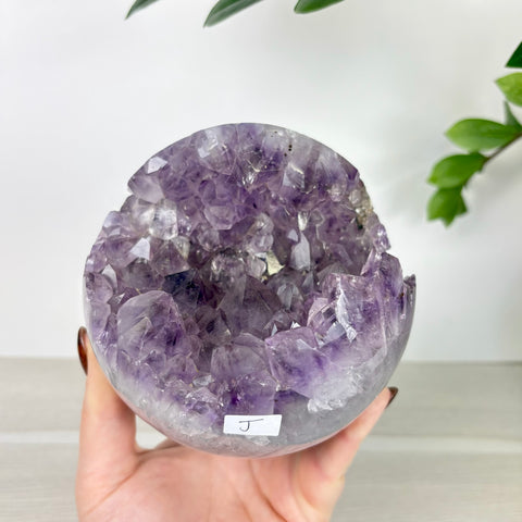 Handheld amethyst geode sphere with deep purple crystals and a smooth agate outer shell.