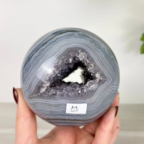 Polished agate sphere with a sparkling amethyst crystal geode center held in a hand.