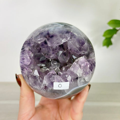 Polished amethyst and agate sphere with a deep, sparkling purple crystal geode center held in a hand.
