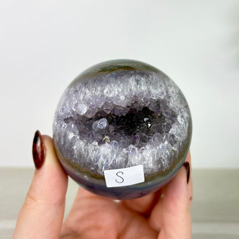 Small amethyst and agate geode sphere with a sparkling purple crystal center held in a hand.