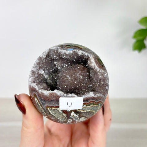Polished amethyst and agate geode sphere with a sparkling purple crystal center held in a hand.