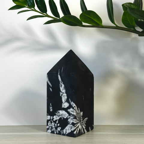 Black Chrysanthemum Stone Tower with white floral patterns, pointed top, on a light wood surface.